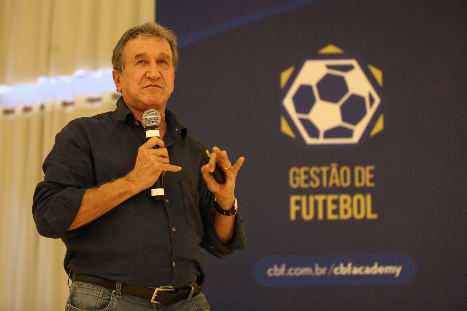 Parreira fala ao microfone durante palestra do curso Gestão de Futebol da CBF Academy, módulo realizado em Teresópolis, com o painel "Gestão de Futebol" da CBF Academy ao fundo.