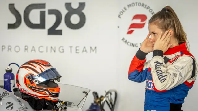 Bruna Tomaselli em seu carro de corrida da NASCAR Brasil, com o capacete e o uniforme de piloto