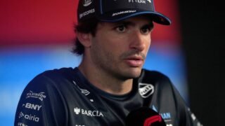 Carlos Sainz em um evento de imprensa da Fórmula 1, sorrindo e falando em um microfone