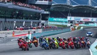 Piloto de MotoGP em alta velocidade na pista de Sepang, na Malásia, com céu nublado antes dos treinos.